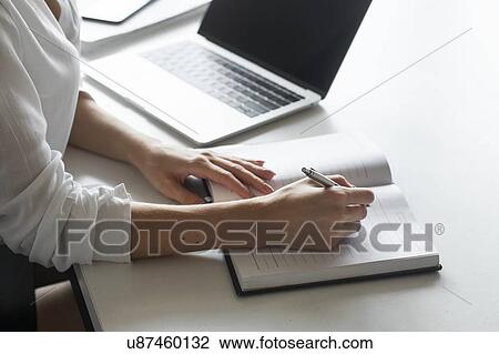Stock Image - Hand of young businesswoman writing notes at desk. Fotosearch