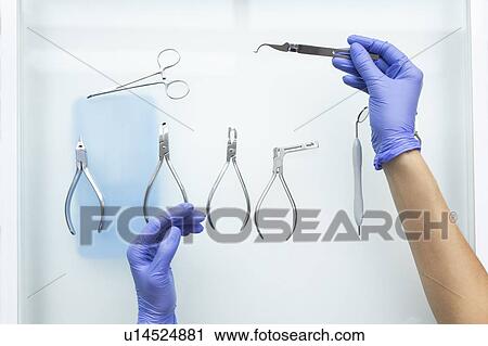 Stock Image - Hands of dental assistant wearing rubber gloves with dental equipment. Fotosearch