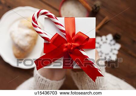 Stock Image - Hands of woman holding Christmas present with candy cane. Fotosearch