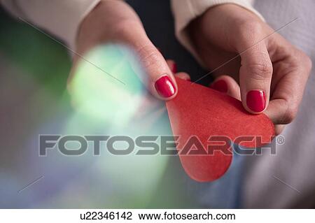 Stock Image - Hands of woman holding red paper heart. Fotosearch