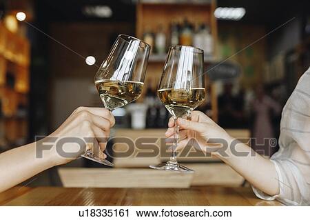Stock Image - Hands of women toasting with glasses of white wine. Fotosearch