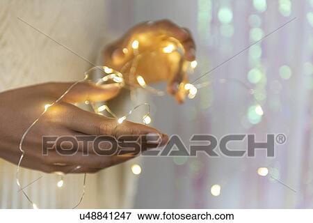 Stock Photo - Hands of young woman holding fairy lights. Fotosearch