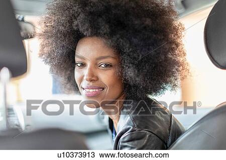 Stock Image - Happy young woman with afro hair in car passenger seat, portrait. Fotosearch