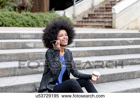 Happy young woman with afro hair sitting on city stairway, listening to smartphone View Large Photo Image Stock Photography - Happy young woman with afro hair sitting on city stairway, listening to smartphone. Fotosearch