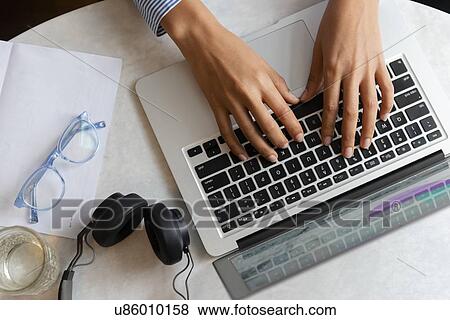 Stock Photo - High angle view of young woman's hands typing on laptop. Fotosearch