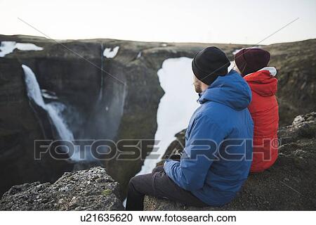 Stock Image - Hiker couple sitting on cliff by Haifoss waterfall in Iceland. Fotosearch