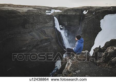 Picture - Hiker sitting on cliff by Haifoss waterfall in Iceland. Fotosearch