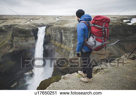 Stock Image - Hiker with backpack on cliff by Haifoss waterfall in Iceland. Fotosearch