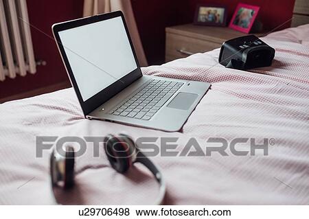 Stock Photo - Laptop, VR headset and headphones on bed. Fotosearch