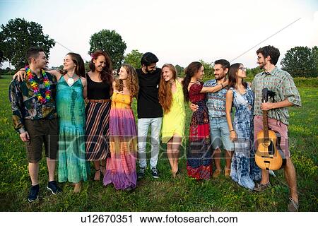 Stock Image - Large group of happy young adults standing in field with arms around each other. Fotosearch