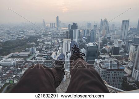 Stock Image - Legs of young man and cityscape of Bangkok, Thailand. Fotosearch