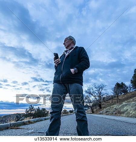 Low angle view of man holding smart phone on road View Large Photo Image Picture - Low angle view of man holding smart phone on road. Fotosearch