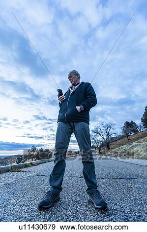 Low angle view of man holding smart phone on road View Large Photo Image Stock Photo - Low angle view of man holding smart phone on road. Fotosearch