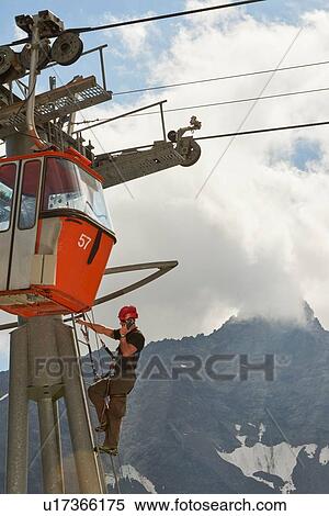 Stock Photography - Maintenance worker climbing up cable car, Saas-Fee, Valais, Switzerland. Fotosearch