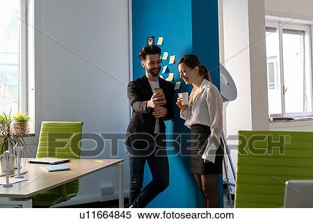Stock Photography - Male and female business creatives taking a break and looking at smartphone in office. Fotosearch