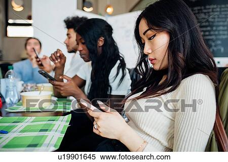 Male and female business team looking at smartphones while having working lunch at cafe table View Large Photo Image Stock Photography - Male and female business team looking at smartphones while having working lunch at cafe table. Fotosearch