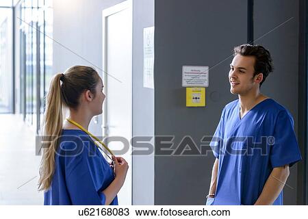 Stock Image - Male and female junior doctors chatting in hospital corridor. Fotosearch