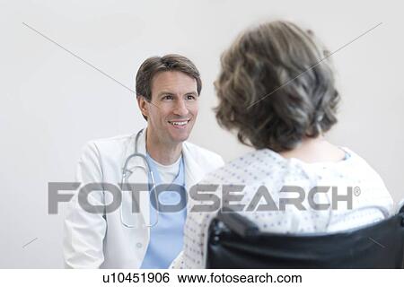 Stock Photograph - Male doctor smiling at mature female patient in wheelchair.. Fotosearch