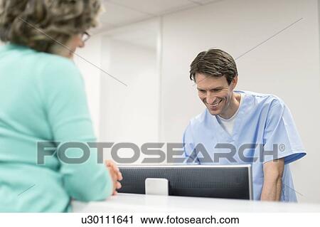 Stock Image - Male nurse using computer with female patient.. Fotosearch