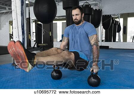 Stock Image - Man balancing on kettlebells in gym. Fotosearch