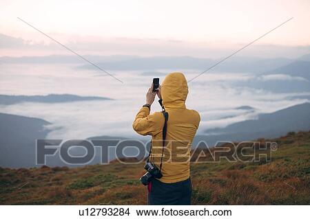 Picture - Man in yellow jacket taking photograph on smart phone in the Carpathian Mountain Range. Fotosearch