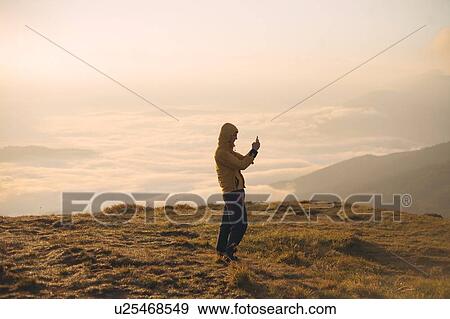 Man in yellow jacket taking photograph on smart phone in the Carpathian Mountain Range View Large Photo Image Stock Photo - Man in yellow jacket taking photograph on smart phone in the Carpathian Mountain Range. Fotosearch
