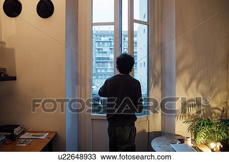 Stock Image - Man looking out of house window. Fotosearch