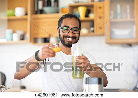 Stock Image - Man making green juice in kitchen. Fotosearch