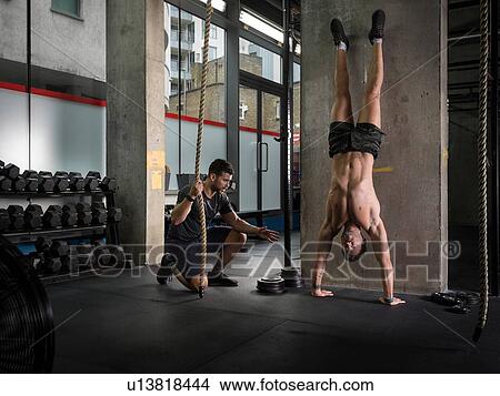 Man motivating friend doing handstand in gym View Large Photo Image Picture - Man motivating friend doing handstand in gym. Fotosearch