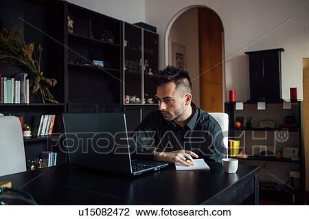 Stock Image - Man using laptop in home office. Fotosearch