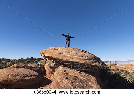 Picture - Man with arms outstretched on rock in Arches National Park, Utah, USA. Fotosearch