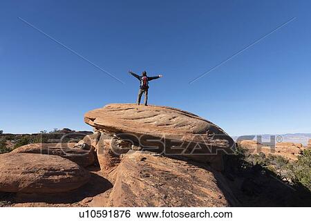 Stock Photograph - Man with arms outstretched on rock in Arches National Park, Utah, USA. Fotosearch