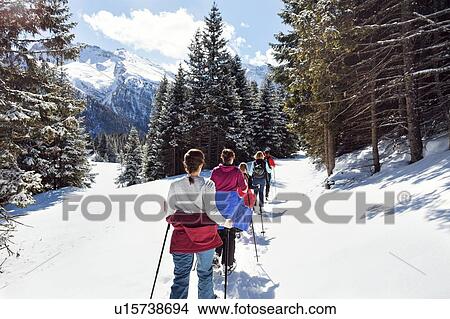 Picture - Mature couple and daughters snowshoeing in snow covered mountain landscape, rear view, Styria, Tyrol, Austria. Fotosearch