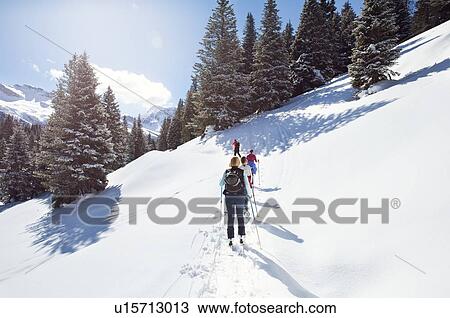 Stock Image - Mature couple and daughters snowshoeing in snow covered mountain landscape, rear view, Styria, Tyrol, Austria. Fotosearch