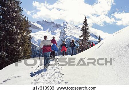 Stock Image - Mature couple and daughters snowshoeing in snow covered mountain landscape, rear view, Styria, Tyrol, Austria. Fotosearch