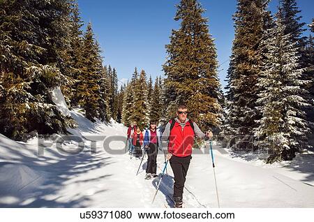 Stock Image - Mature couple and daughters snowshoeing in snow covered forest landscape, Styria, Tyrol, Austria. Fotosearch