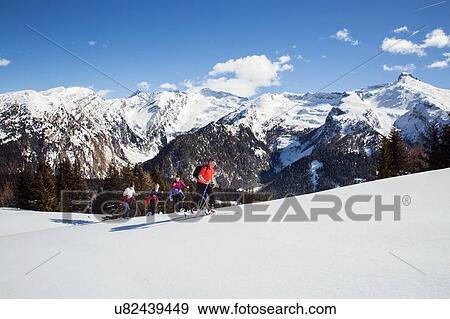 Stock Photo - Mature couple and daughters snowshoeing uphill in snow covered mountain landscape, Styria, Tyrol, Austria. Fotosearch