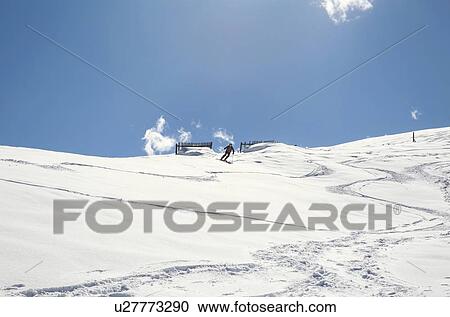 Stock Image - Mature man skiing down snow covered mountain, distant low angle view, Styria, Tyrol, Austria. Fotosearch