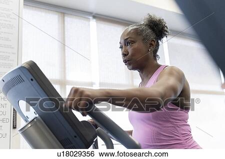 Stock Photograph - Mature woman exercising on elliptical machine. Fotosearch