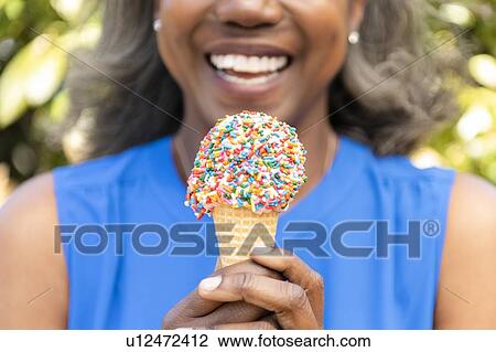 Stock Image - Mature woman holding ice cream cone with sprinkles. Fotosearch