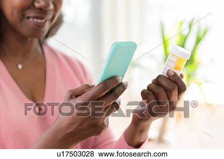 Stock Photo - Mature woman holding smart phone and medicine bottle. Fotosearch