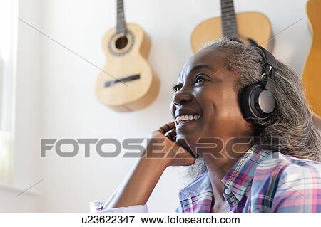 Stock Photo - Mature woman listening to music on headphones. Fotosearch