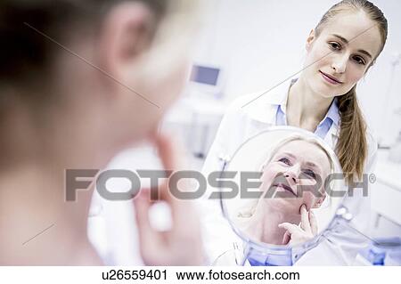 Mature woman looking into a mirror while female doctor standing behind. View Large Photo Image Stock Image - Mature woman looking into a mirror while female doctor standing behind.. Fotosearch