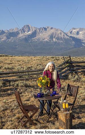 Mature woman setting dining table in field by mountain in Stanley, Idaho View Large Photo Image Stock Image - Mature woman setting dining table in field by mountain in Stanley, Idaho. Fotosearch