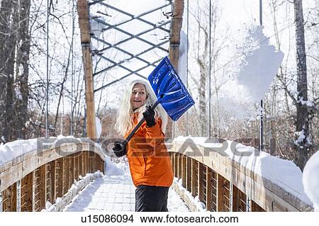 Picture - Mature woman shoveling snow off of footbridge. Fotosearch