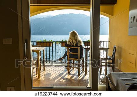Picture - Mature woman sitting on balcony by Lake Como in Lombardy, Italy. Fotosearch