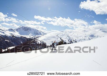 Stock Image - Mature woman snowshoeing up snow covered mountainside, distant view, Styria, Tyrol, Austria. Fotosearch