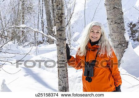Mature woman wearing orange coat by bare trees in snow View Large Photo Image Picture - Mature woman wearing orange coat by bare trees in snow. Fotosearch