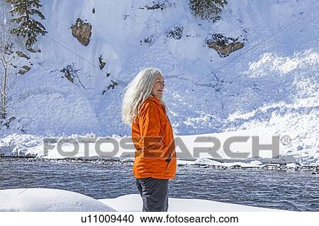 Mature woman wearing orange coat on snow by river View Large Photo Image Stock Image - Mature woman wearing orange coat on snow by river. Fotosearch