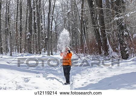 Mature woman wearing orange coat throwing snow by bare trees View Large Photo Image Picture - Mature woman wearing orange coat throwing snow by bare trees. Fotosearch